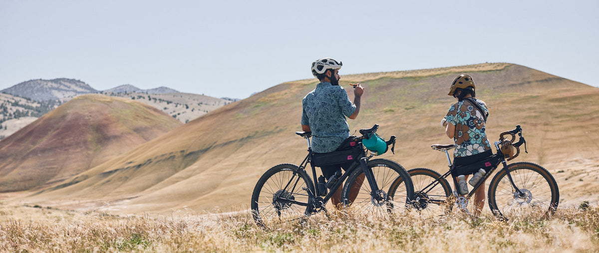Two people sat by their bikes, looking out on a wide landscape
