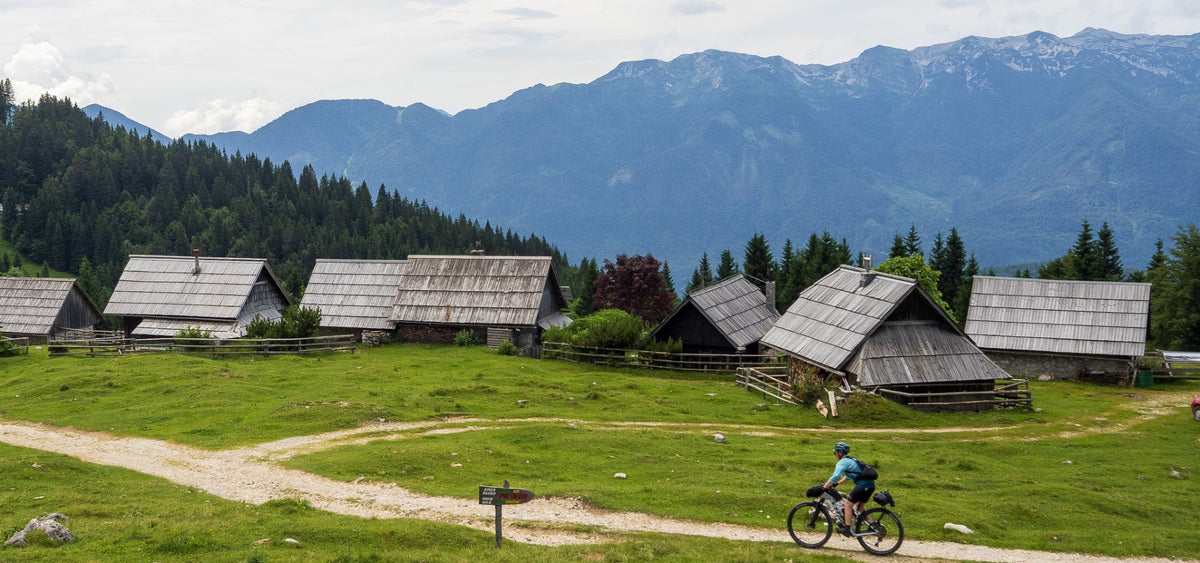 A woman bikepacking through European countryside, with a mountain range in the background