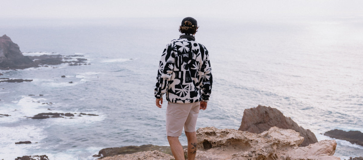A man looking out over the sea, standing on a cliff, wearing a black and white patterned fleece