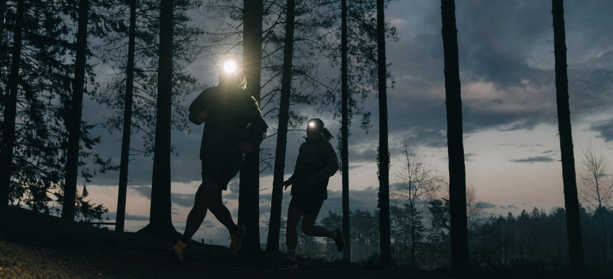 Two people running in a forest at sunrise with head torches on