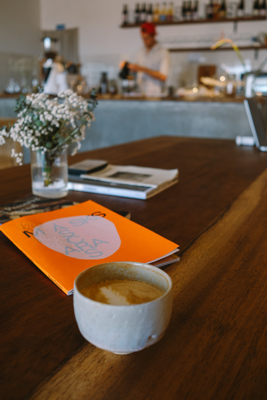 Cup of coffee on a wooden table with a magazine and flowers in the background