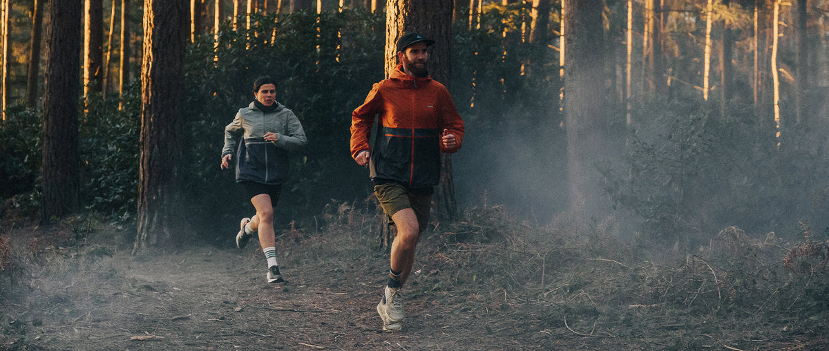 Two trail runners, through a forest in low light