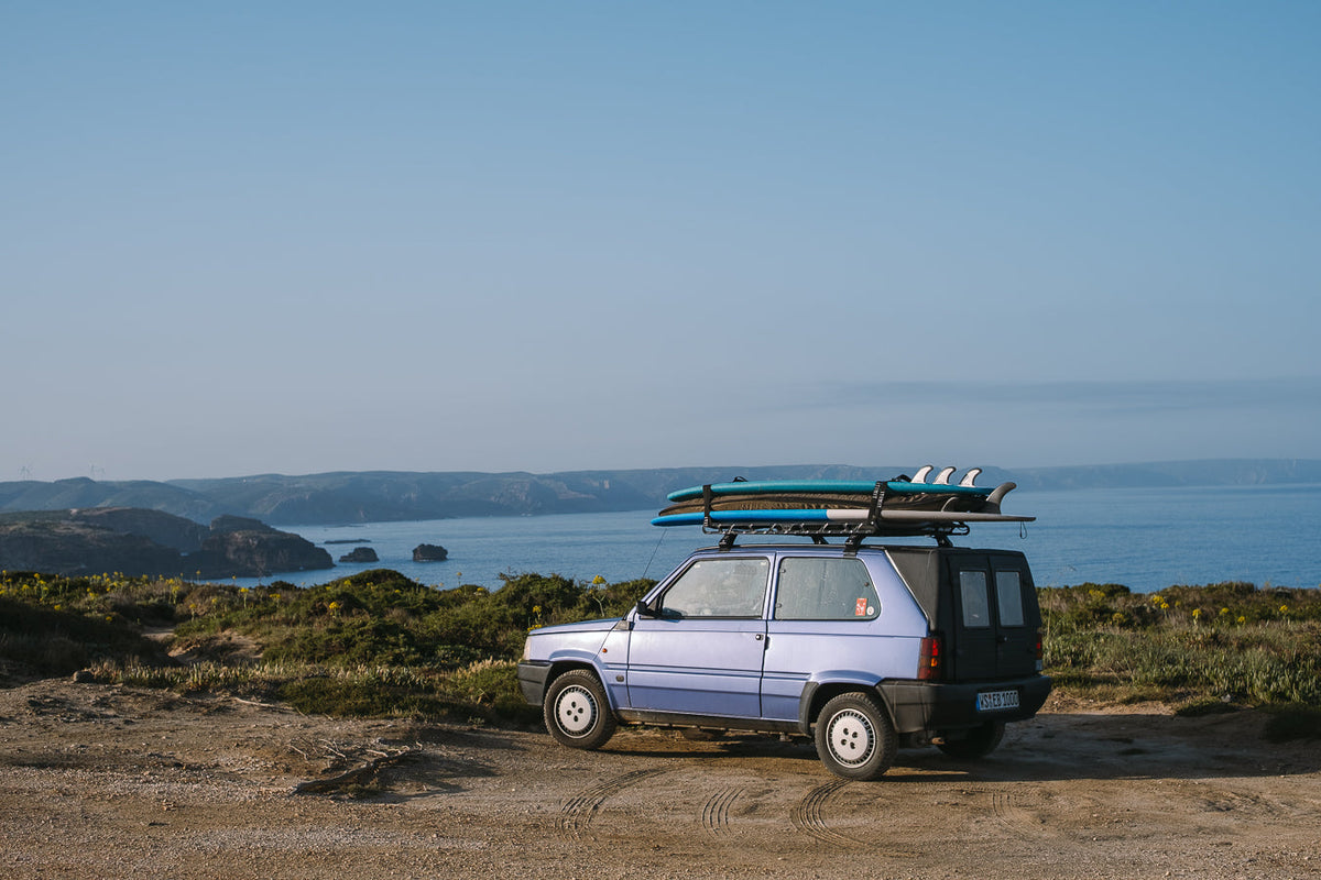 A Fiat Panda with surf boards on the roof rack parked on a cliff overlooking the ocean in Portugal