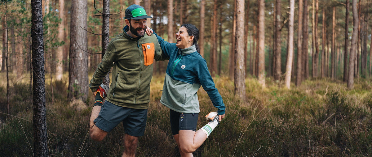 Two people stretching in the woods, prepping for a trail run