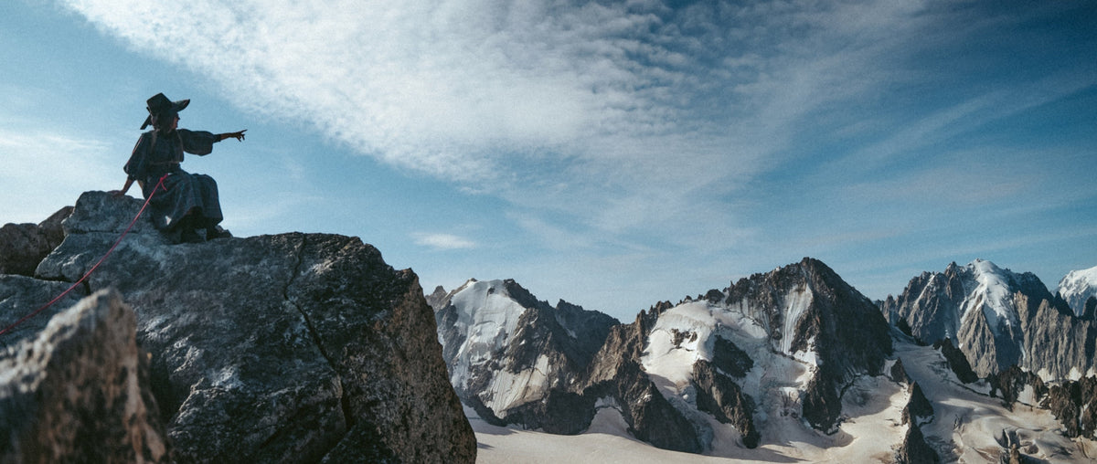 A woman sits on a rock amongst the Alps, pointing out at the view
