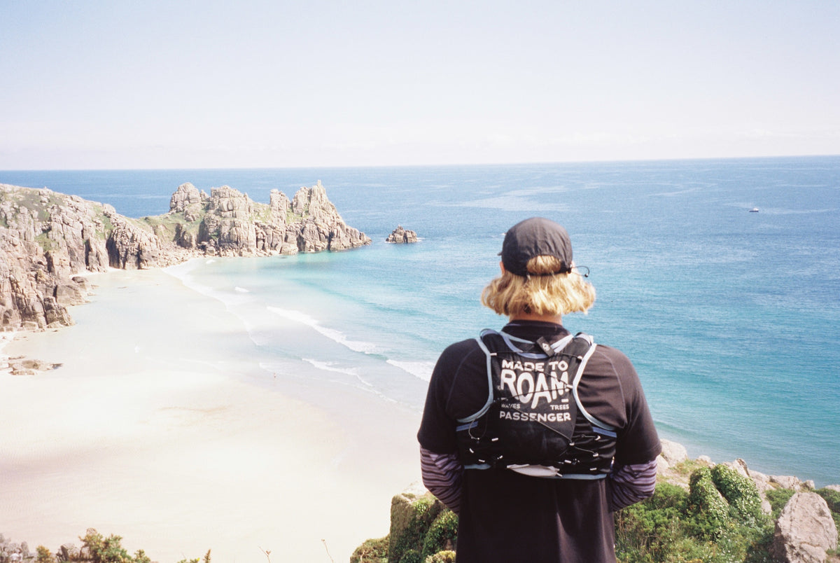 Person wearing a black jacket with 'Made to Roam' branding overlooking a scenic coastal view.