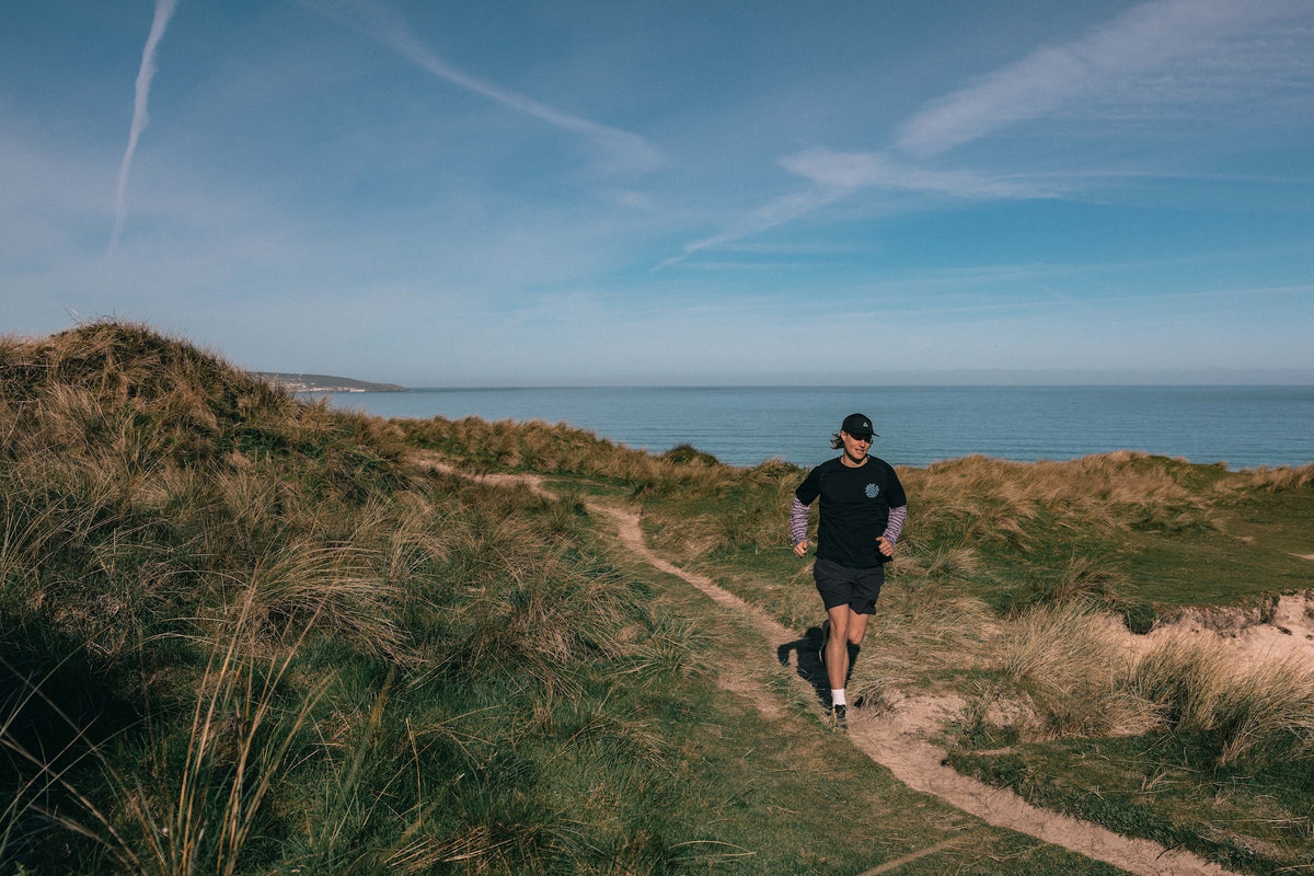 Person running on a path near the ocean with a clear blue sky.